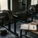 Sporter onder een barbell in een squatrek met een trainingslogboek en pen op de bank ernaast